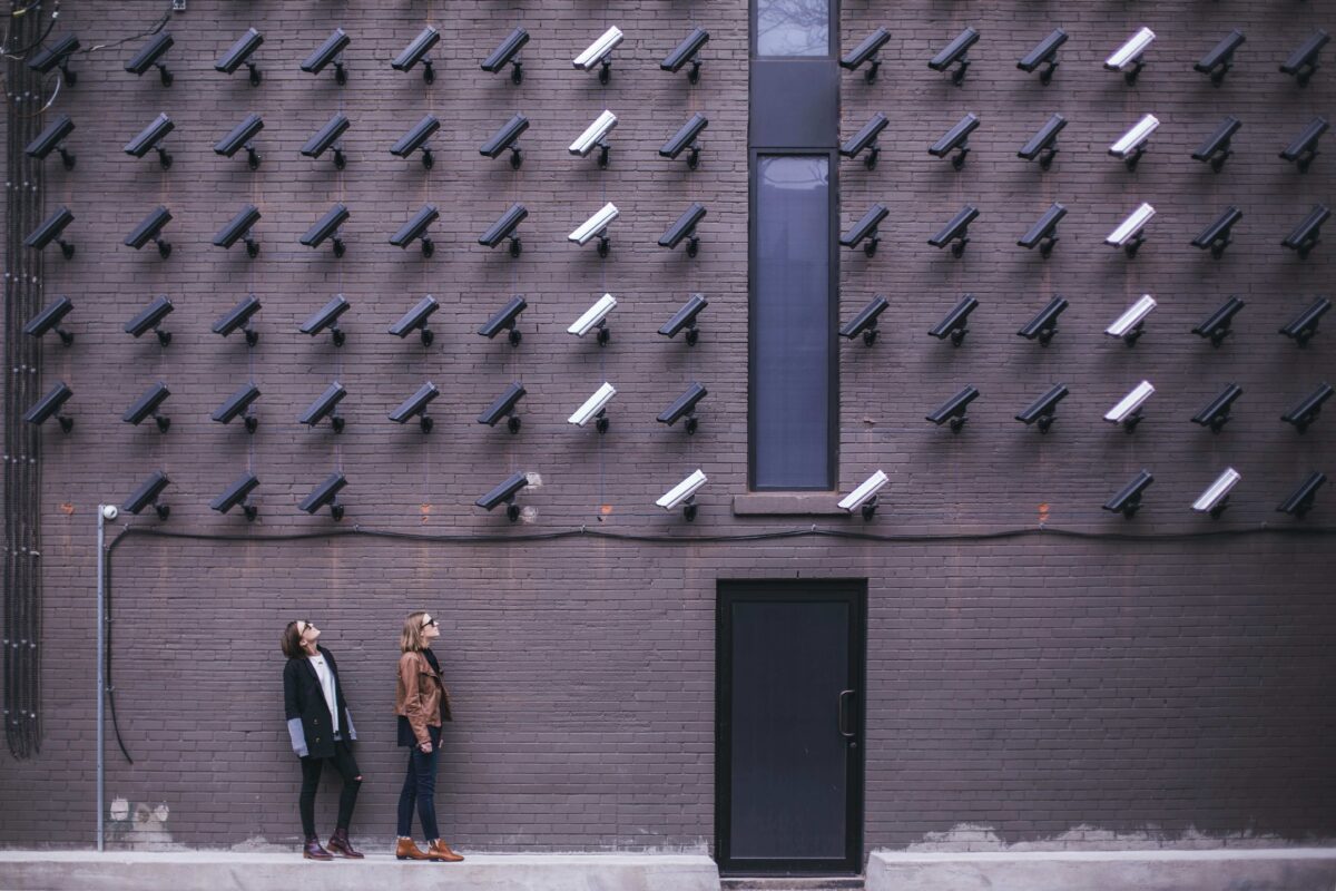 matthew-henry-fPxOowbR6ls-unsplash-new Two people looking up at a brick wall of surveillance cameras